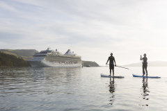 Craig Latta and Di Brenssell ride stand-up paddleboards on the Otago Harbour as a cruise ship Marina heads towards Port Chalmers, Dunedin, New Zealand.