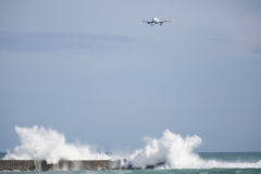 An Air New Zealand plane flies over as swell crashes into a breakwall at Lyall Bay, Wellington, New Zealand.